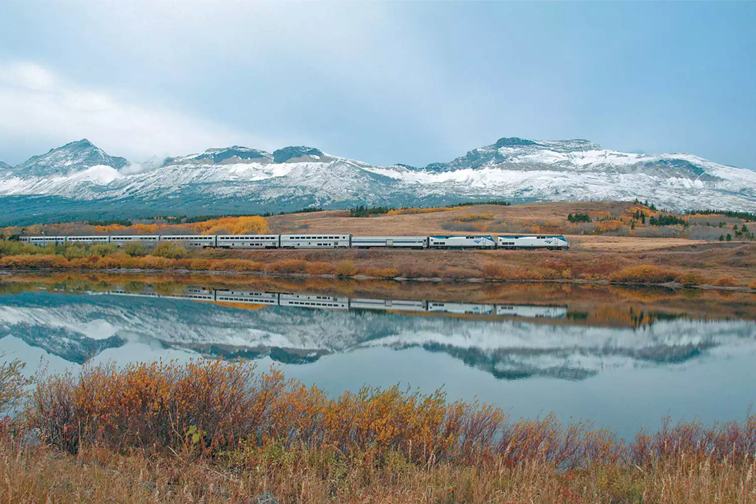 View of Amtrak's Empire Builder going along snow capped mountains and fall foliage 