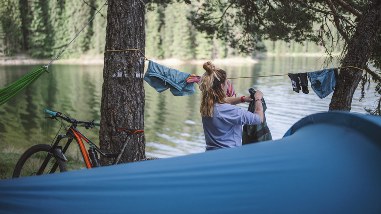 Une femme suspend du linge dans un campement au bord d'une rivière