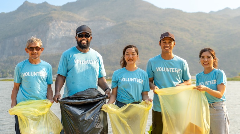 Bénévoles souriants avec des sacs poubelles sur la plage