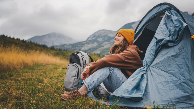 une femme campant en solo, assise à l'entrée de sa tente et profitant de l'air frais et de la solitude