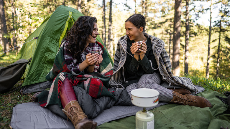 deux campeuses assises devant une tente, buvant du café et riant