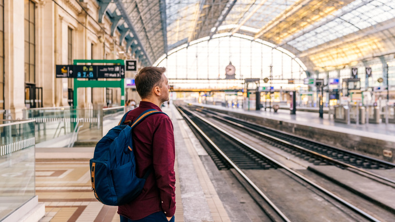 Un jeune homme avec un sac à dos attend sur le quai d'une gare