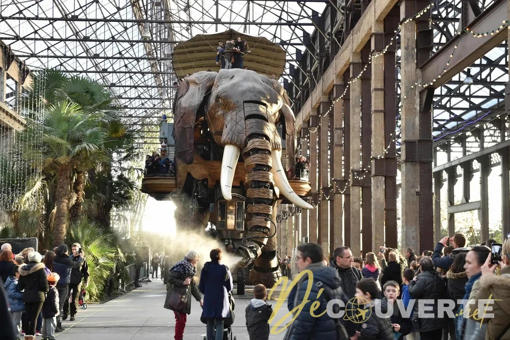 Le Grand Éléphant mécanique sous une charpente métallique, entouré de visiteurs.